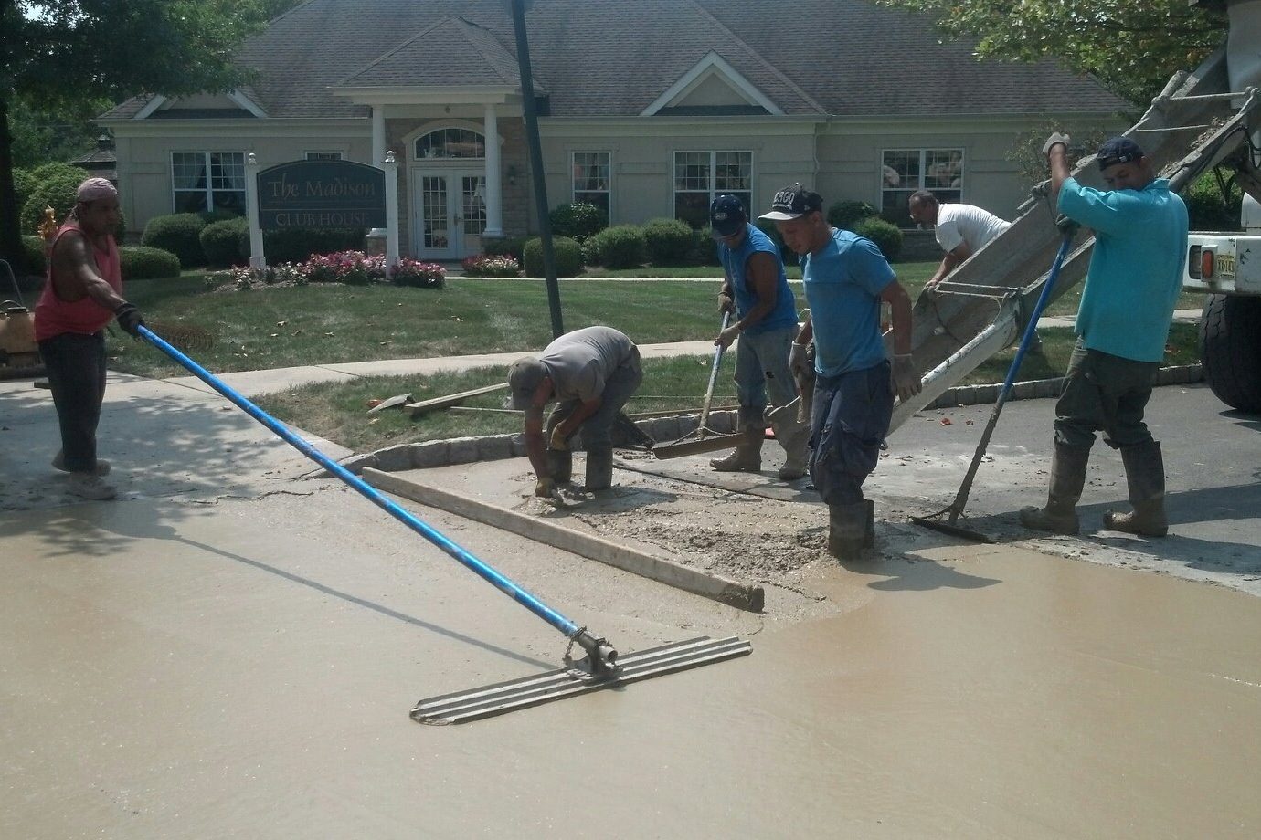 Concrete crew using a long-handled bull float and hand tools to level a fresh concrete pour