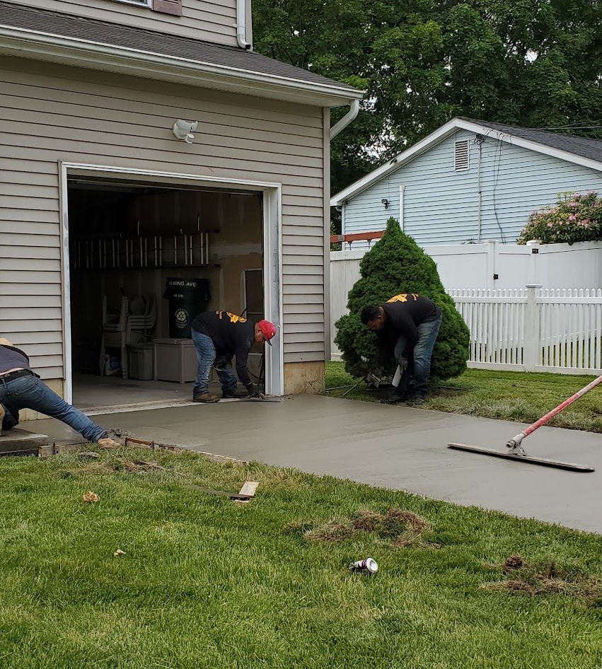 Workers finishing freshly poured concrete in front of an open garage door