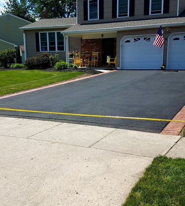 Freshly paved asphalt driveway taped off in front of a two-car garage, with an American flag on the porch
