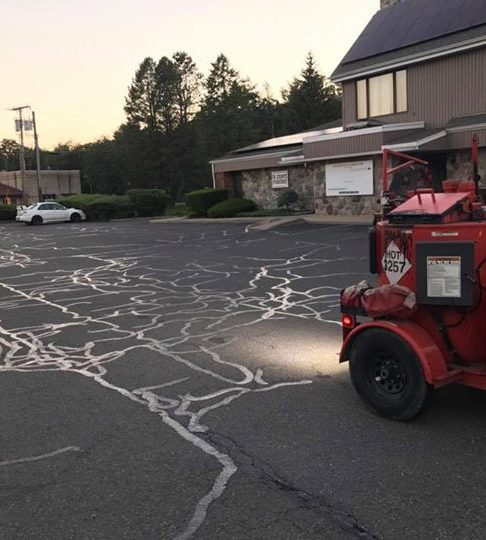 Parking lot with cracks filled with light-colored sealant next to a red crack-sealing machine