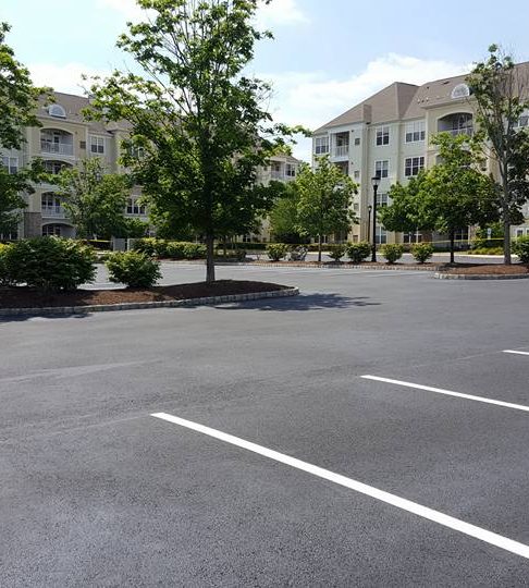 Newly paved black asphalt parking lot with bright white stall lines in front of apartment buildings