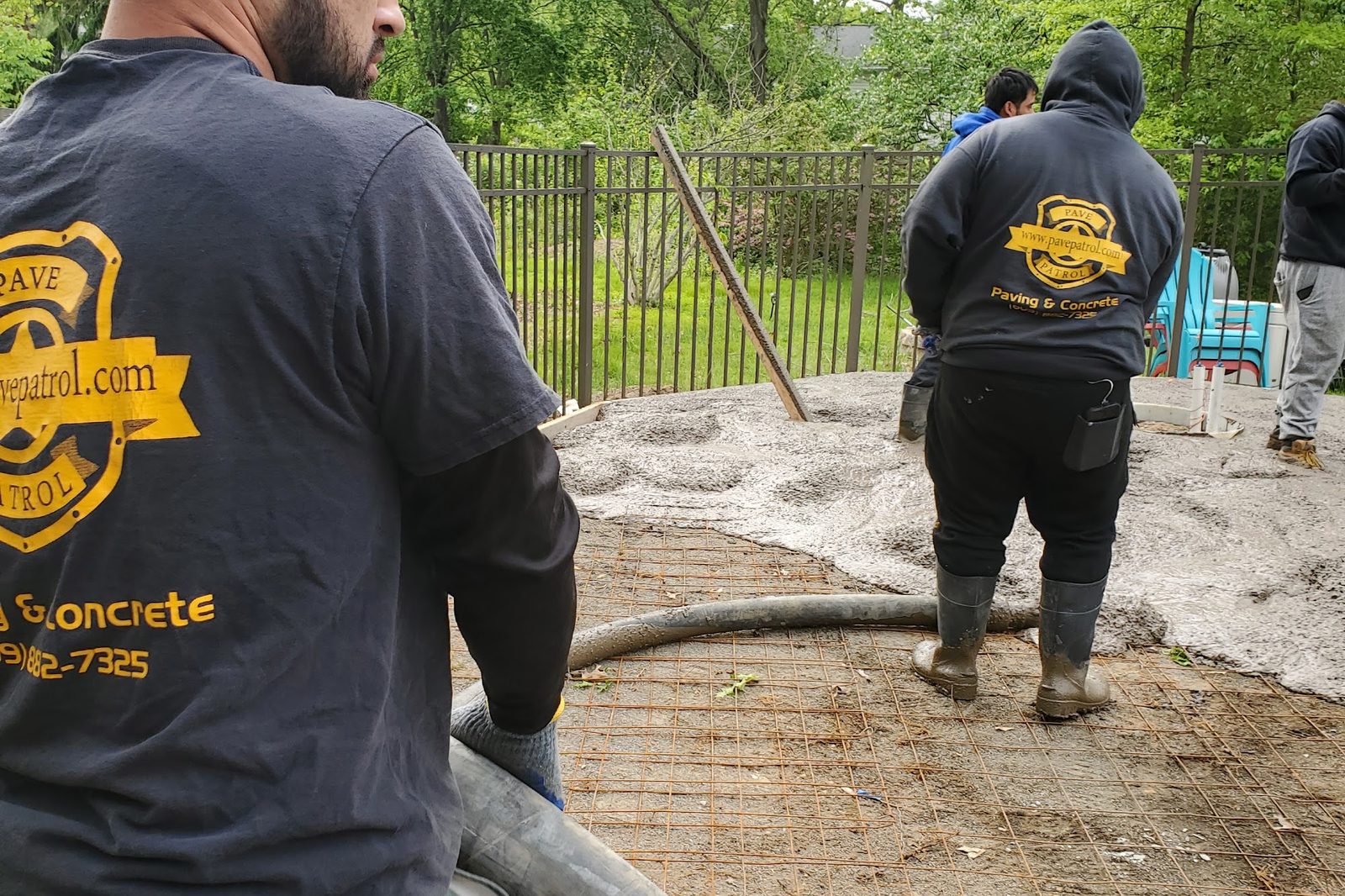 Pave Patrol crew members in branded shirts guiding a concrete pump hose over a prepared base