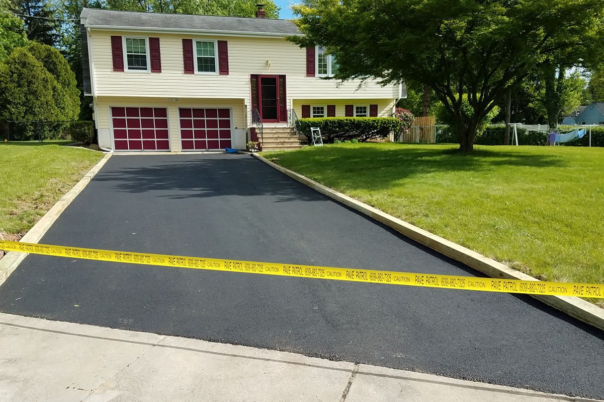 Newly paved asphalt driveway with caution tape across it, leading to a house with red garage doors