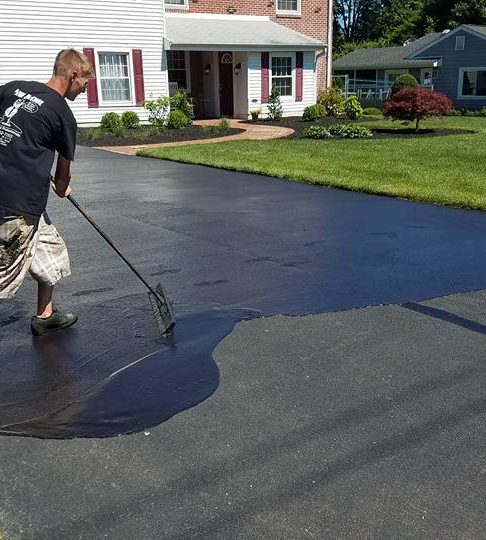 Worker spreading black sealcoat across an asphalt driveway with a squeegee