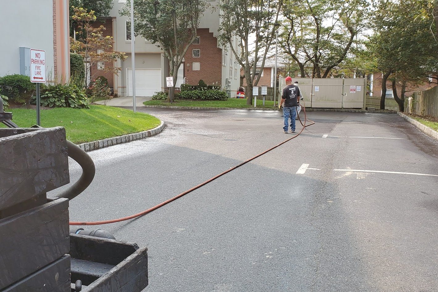 Sealcoat hose stretched across an asphalt lot at a townhome community, worker in the distance