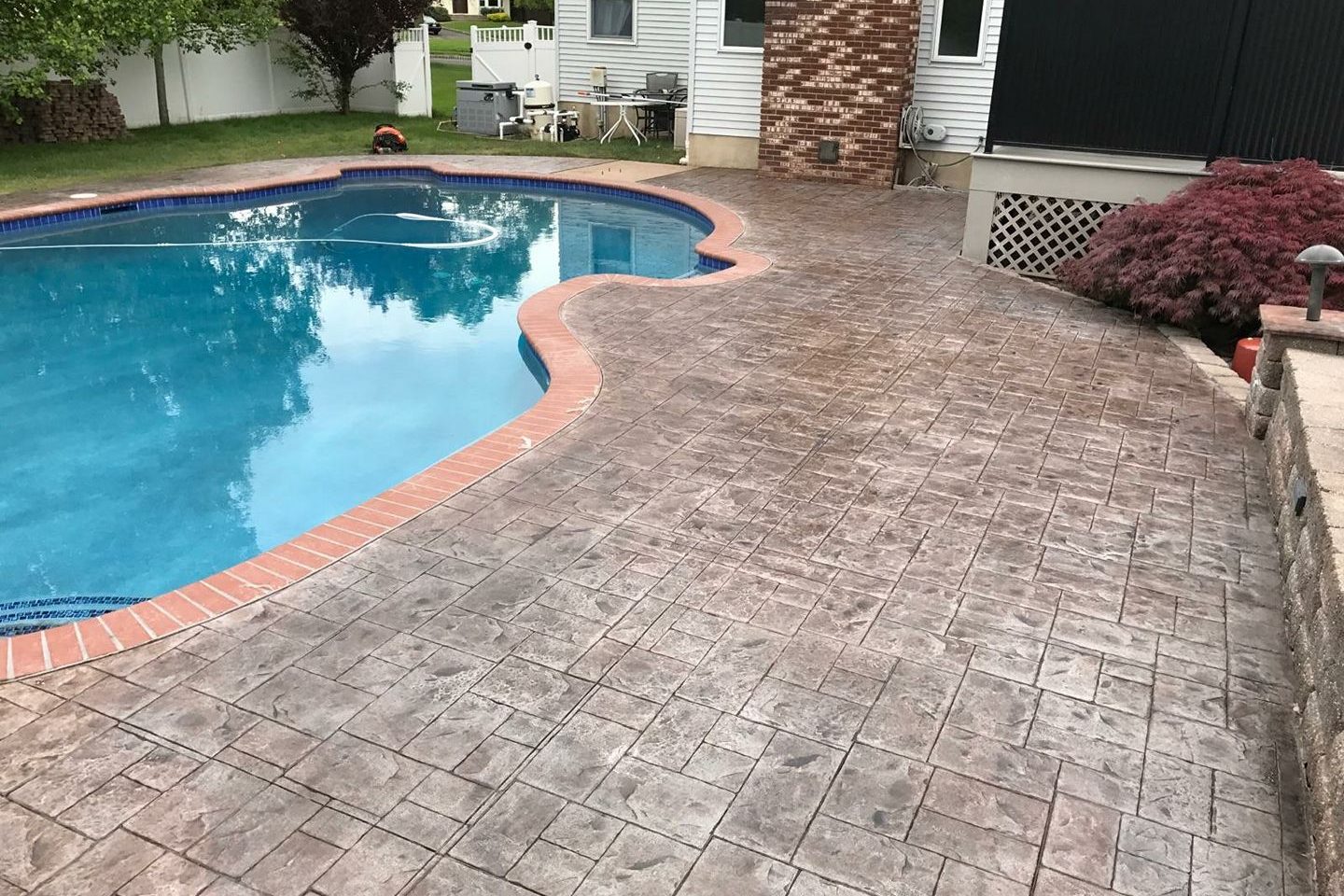 Stamped concrete pool deck surrounding a kidney-shaped pool with brick-colored coping