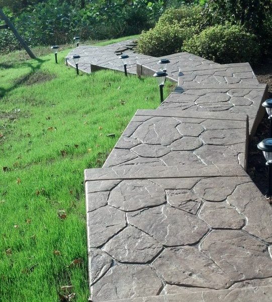 Stamped concrete stone-pattern wall and steps running up a grassy slope, lined with path lights