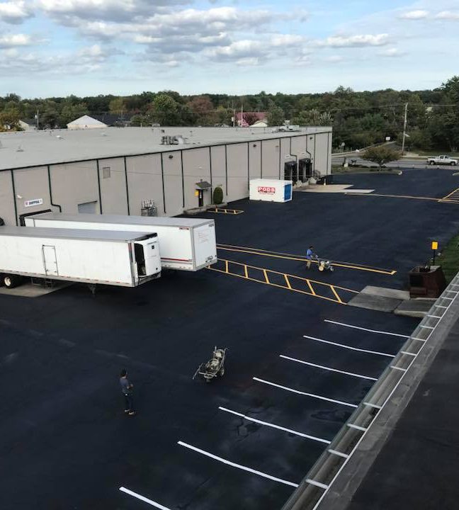 Aerial view of a freshly paved and striped commercial lot beside a warehouse with parked trailers